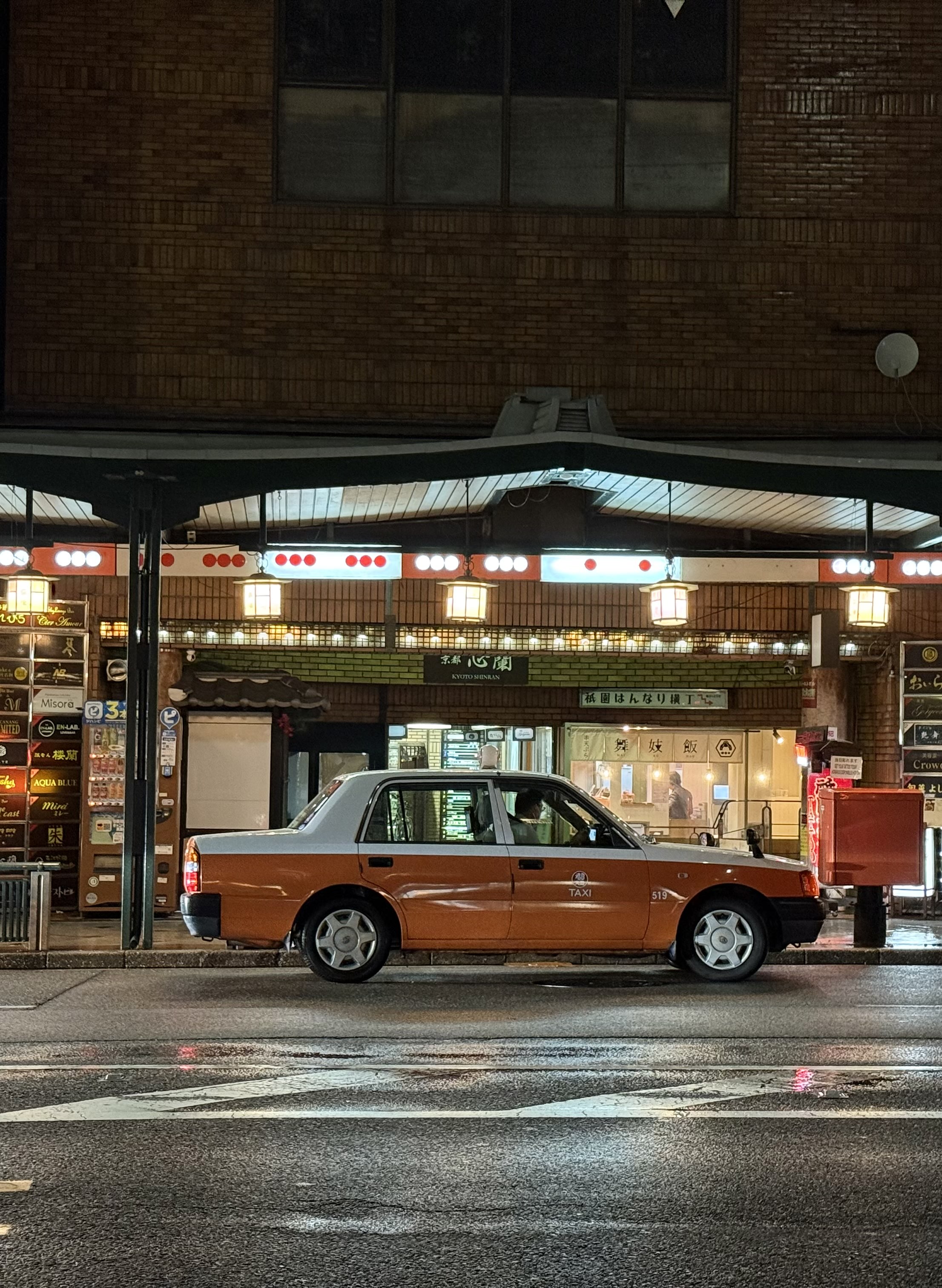 A orange still Taxi on a busy neon lit street with high reflections